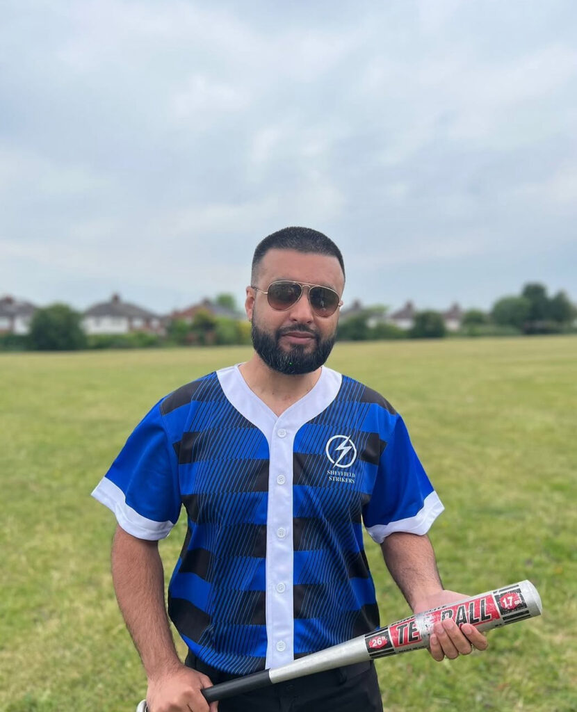 Photo of a man - Nomaan Iqbal - holdingj a baseball bat in a field